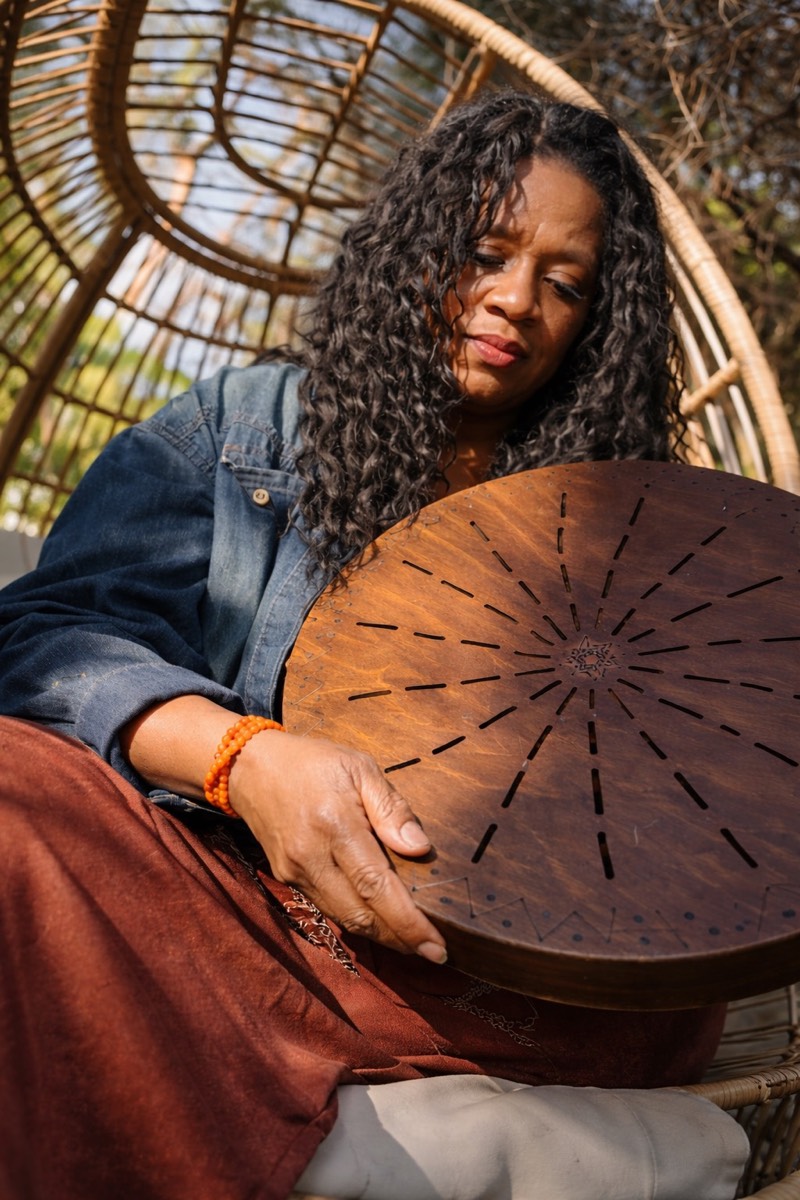 Nea, Sister Red Hawk, seated in a rattan chair holding her sun drum